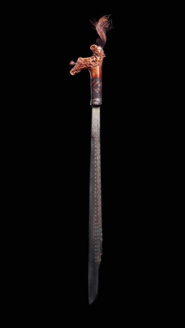 Dayak Mandau Headhunter Sword with Carved Bone Aso Hilt, 19th C.: Southeast Asia, Borneo, Kalimantan, Dayak, ca. 1800–1899 CE. A headhunter's mandau whose polished blade curves to a lifted point, its convex face inlaid with brass "matah joh" roundels and s-scr