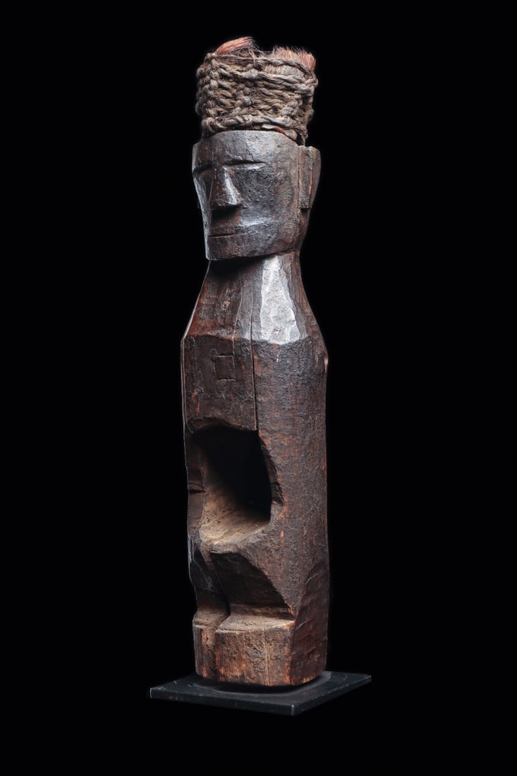 Batak Pagar Medicine Figure with Fiber Headdress, 19th C. or Earlier: Southeast Asia, Sumatra, Indonesia, Batak, ca. 1800–1900 CE. A gaunt ancestor figure hewn from dense hardwood, columnar in build, its wide planar face reduced to a ridged brow, wedge nose, and s