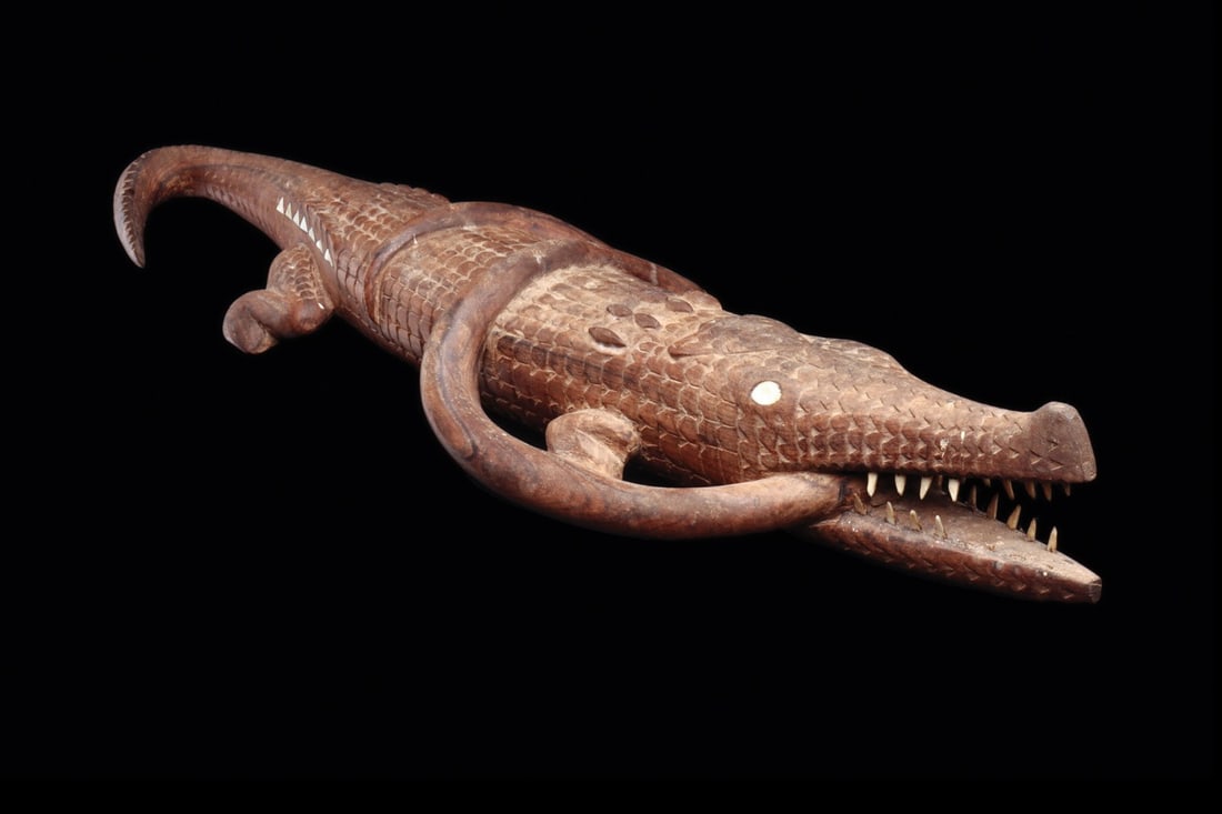 Solomon Islands Carved Wood Crocodile and Serpent, 19th-20th C.: Melanesia, Solomon Islands, ca. 1850–1950 CE. A hardwood crocodile stretched out in mid-hunt, jaws parted on a bristling set of inset bone teeth while a slender serpent loops twice around its bo