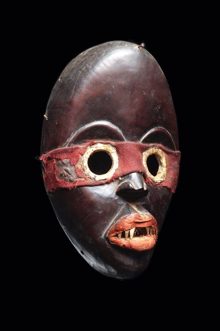 Dan Zakpai Style Mask with Metal-Rimmed Eyes and Red Cloth Band: West Africa, Ivory Coast, Dan culture, ca. 1900–1960 CE. A carved wooden face mask of the northern Dan type, possibly a Zakpai fire-watcher mask. The high domed forehead sweeps into an ovoid fac