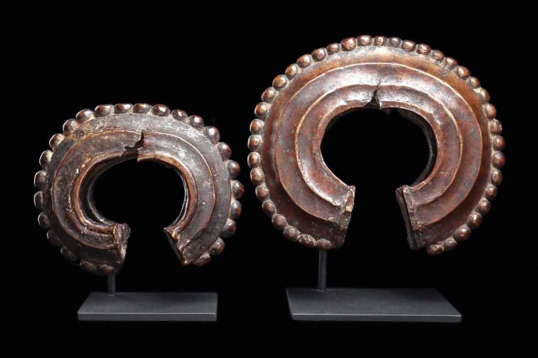 Dan or We Guere Anklets, Pair, Noded C-Form Prestige Currency, West Africa: West Africa, Ivory Coast / Liberia, Dan or We Guere, ca. 1880–1950 CE. A pair of massive cast anklets, each a hollow C of copper alloy whose outer edge is ringed with bold spherical nodes like a
