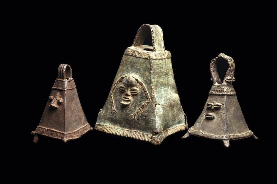 Owo Yoruba Copper Alloy Bells with Faces, Group of Three: West Africa, Nigeria, Owo Yoruba, ca. 1400–1900 CE. A trio of cast bells of tapering pyramidal form, each rising to an arched strap handle above a flaring, textured basal band. Human faces emerg