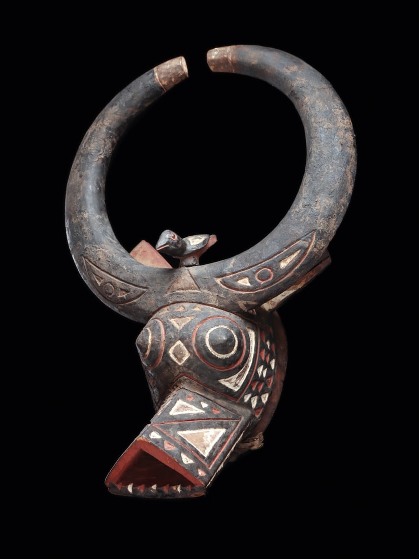 Nuna or Bwa Buffalo Mask with Oxpecker Bird, Burkina Faso, 20th C.: West Africa, Burkina Faso, Nuna or Bwa peoples, ca. 1900–1975 CE. A buffalo mask whose vast crescent horns sweep upward into a near-closed ring, framing an oxpecker bird perched alert on the ani