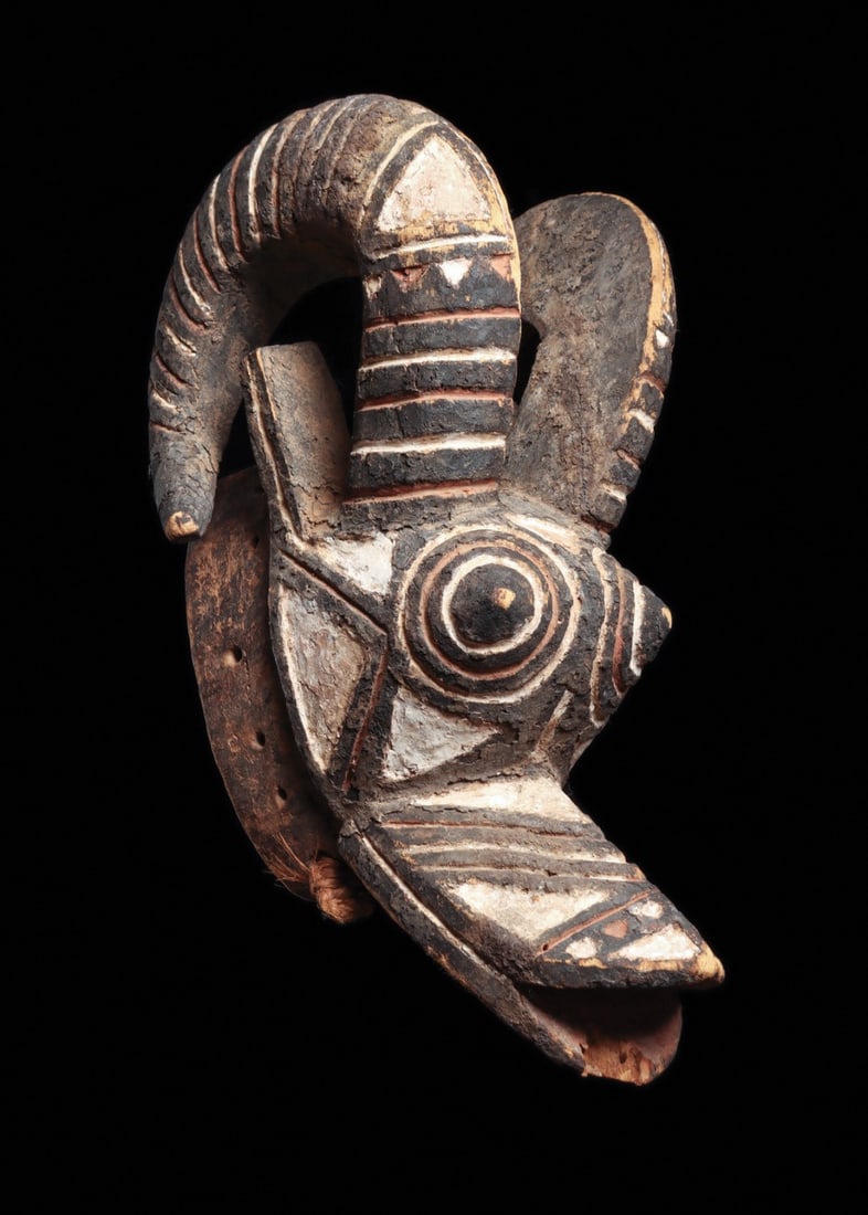 Nunuma Ram Mask with Curved Horns, Burkina Faso, 20th C.: West Africa, Burkina Faso, Nunuma culture, ca. 1900–1975 CE. A ram rendered in wood with unapologetic force: sweeping horns curl back from the crown, concentric-ringed eyes bulge above a long pr