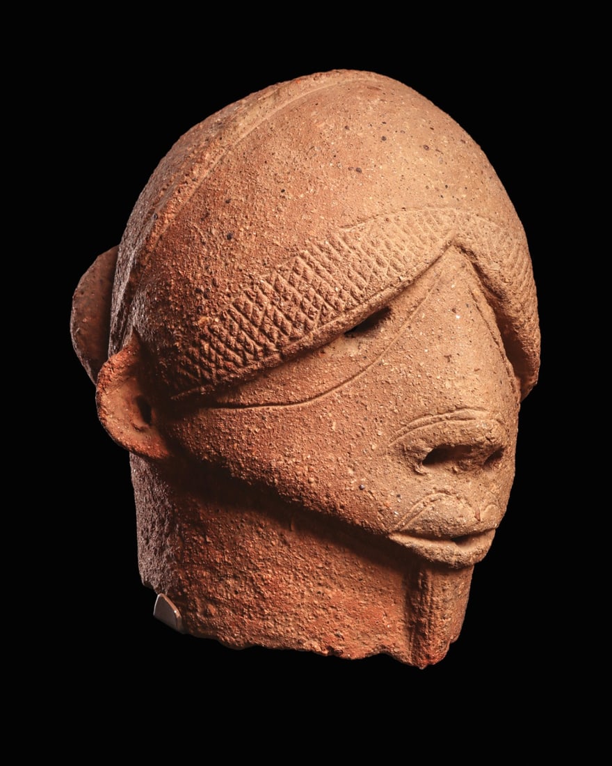 Sokoto Terracotta Head of a Bearded Dignitary: West Africa, Nigeria, Sokoto culture, ca. 500 BCE – 500 CE. A hollow-built head of gray-brown terracotta, near lifesize, portraying a bearded man of evident rank. The heavy-lidded eyes are carve