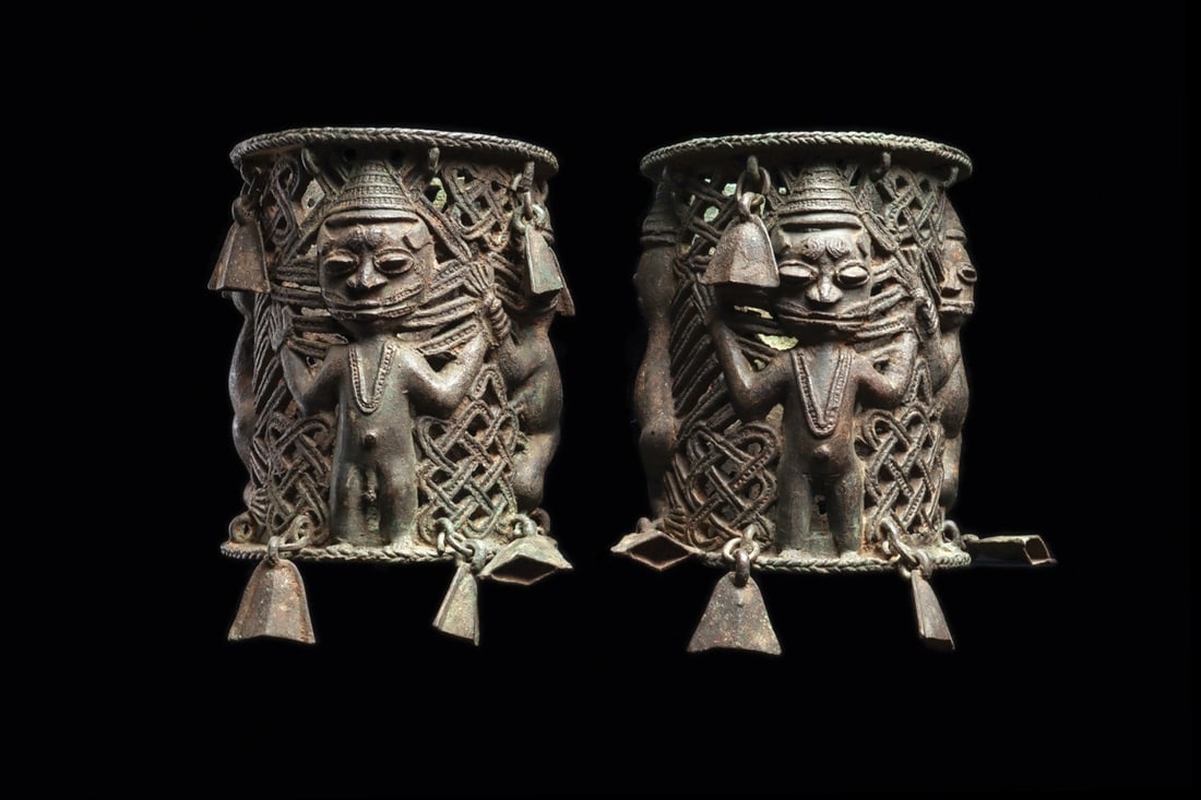 Yoruba Ogboni Society Bracelet Pair with Figures and Bells, Ijebu: West Africa, Nigeria, Ijebu region, Yoruba, ca. 1875–1950 CE. A matched pair of cylindrical openwork cuffs cast in a copper alloy, each built around four figures in high relief: a frontal standi