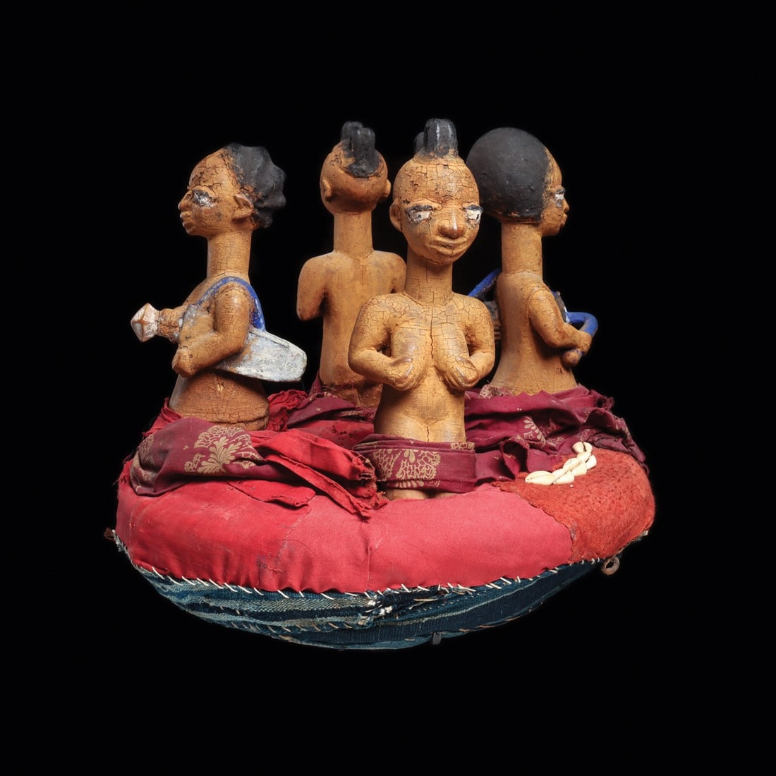 Yoruba Egungun Headdress with Four Figures, Drummer and Kneeling Women: West Africa, Nigeria, Yoruba, ca. 1900–2000 CE. A padded disc crown of layered red, maroon, and indigo cloth, hand-stitched at the rim and studded with rows of sewn cowrie shells, carries four c