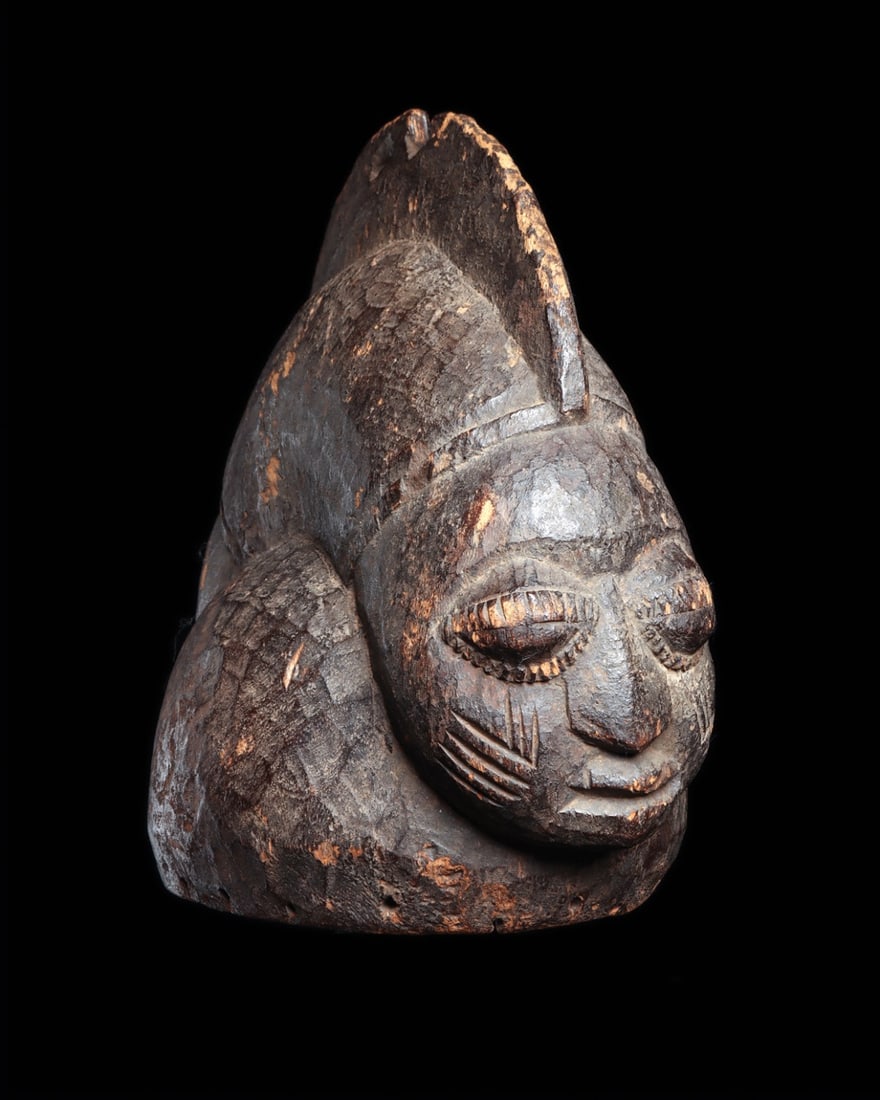Yoruba Egungun Janus Helmet Mask with Sagittal Crest: West Africa, Nigeria, Yoruba, ca. 1900–1960 CE. A hemispherical helmet carved from a single block of hardwood, presenting two opposing faces divided by a tall sagittal crest. Each visage is comp