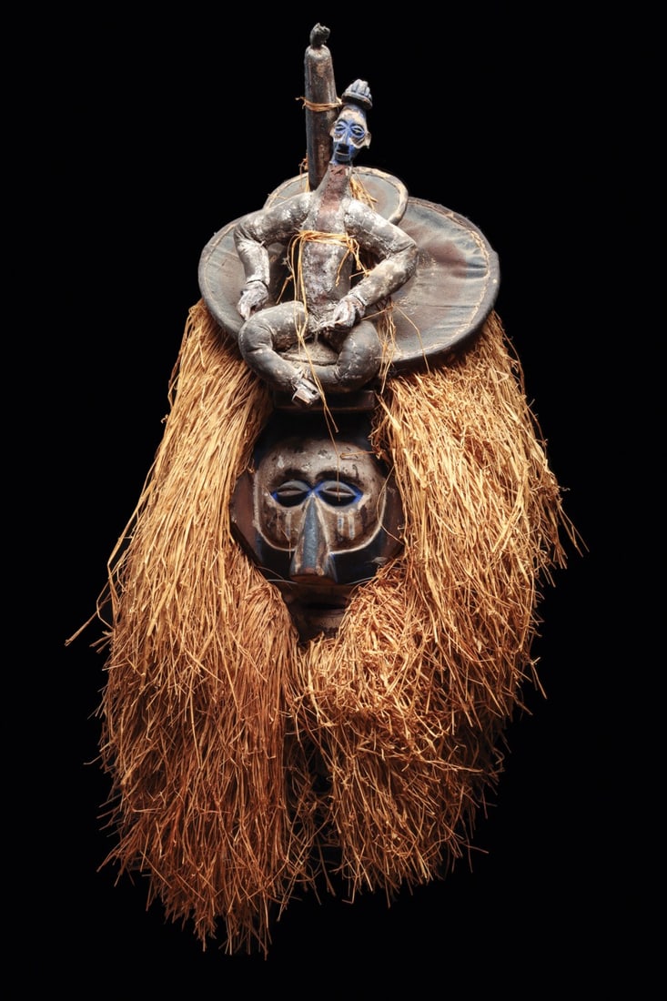 Yaka Initiation Mask with Seated Figure Superstructure and Raffia Mane: Central Africa, Democratic Republic of the Congo, Yaka, ca. 1930–1980 CE. “Kholuka” helmet mask, a striking ceremonial mask worn during initiation rites. The large wooden mask is sur