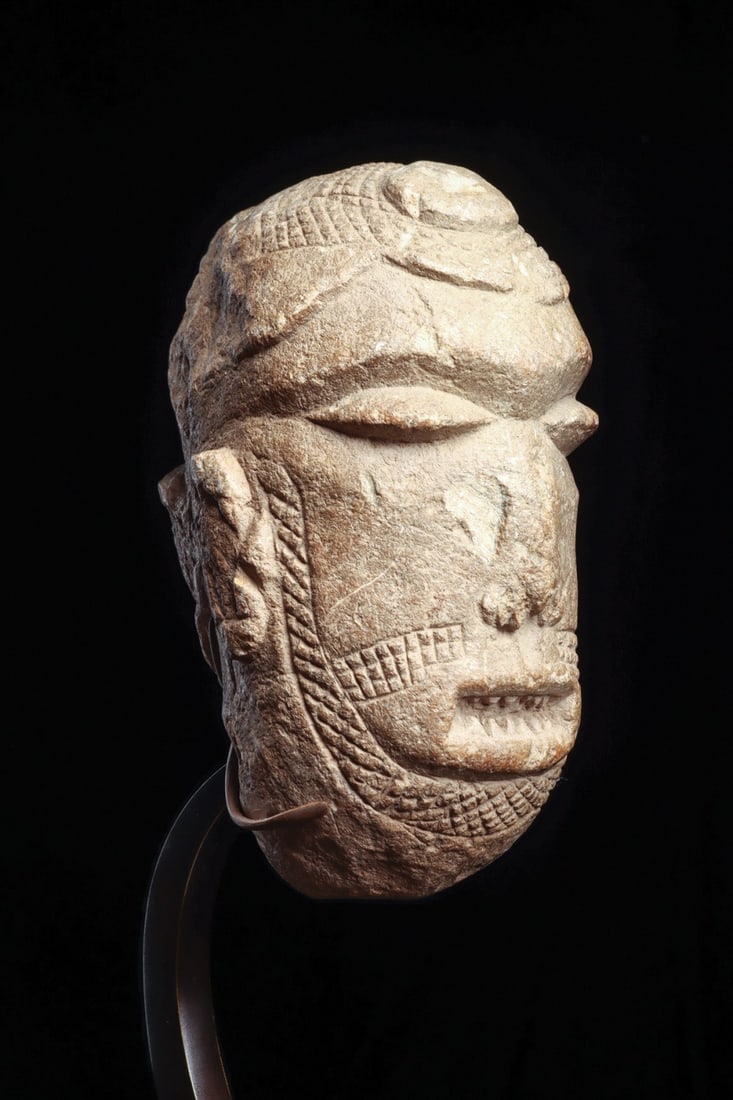 Sapi Mahen Yafe Stone Head, Sierra Leone, 15th-19th C.: West Africa, Sierra Leone, Sapi culture, ca. 1400–1899 CE. A heavy ovoid head carved from tan stone, probably soapstone, its features held in a broad, inward calm. The lids are lowered over swel