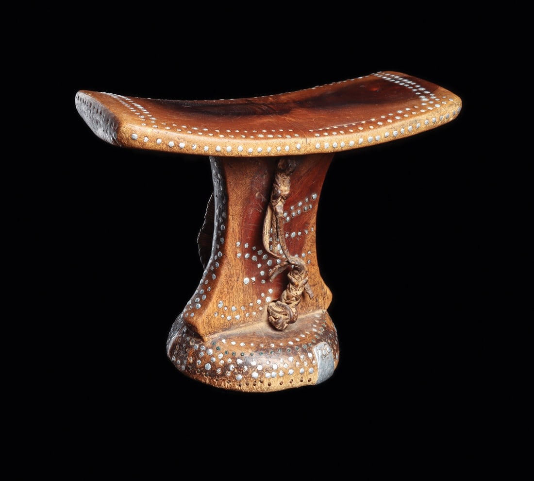 Turkana Headrest with Metal Stud Inlay and Leather Carrying Strap, Kenya: East Africa, Kenya, Turkana peoples, ca. 1900–1960 CE. A carved hardwood headrest whose gently dished rectangular platform rides on a waisted pillar and domed foot. Rows of white metal studs pun