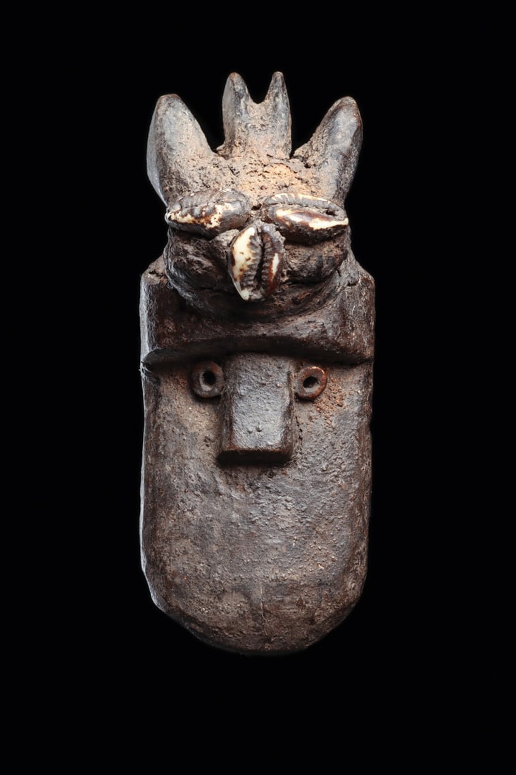 Toma Miniature Passport Maskette with Cowrie Fetish Bundle, Liberia: West Africa, Liberia, Toma (Loma), ca. 1900–1960 CE. A miniature carved wood maskette of the personal, small-scale type associated with Poro society usage. The elongated face is reduced to essen