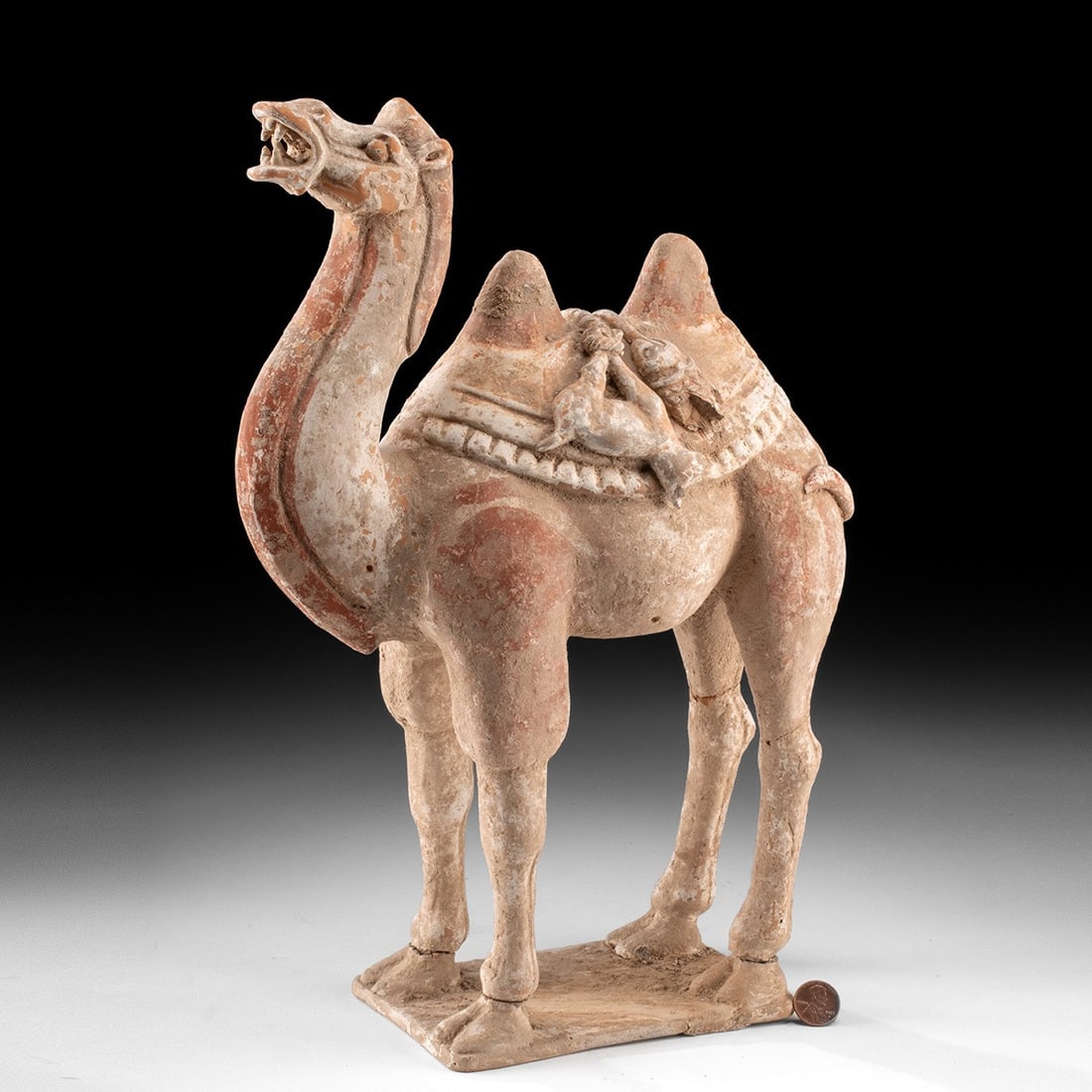 Chinese Han Dynasty Pottery Bactrian Camel, TL Tested: Chinese Han Dynasty, ca. 202 BCE – 220 CE. A pottery Bactrian camel figure in red clay, standing on an integral plinth with the head raised and mouth open. The camel wears a fringed blanket and 