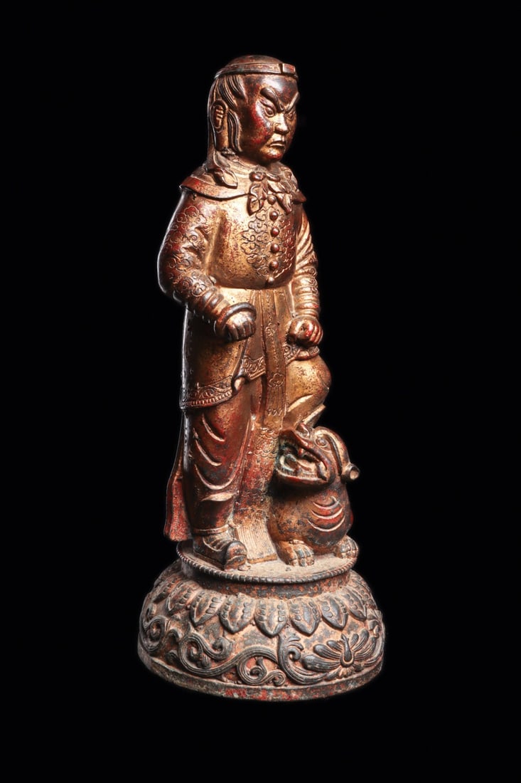 Ming Dynasty Gilt Figure of a Guardian with Lion, 17th C.: East Asia, China, Ming Dynasty, 1644 CE. A cast figure of a standing dignitary, robed and belted, one foot advanced over the back of a crouching Buddhist lion. The long tunic is worked in low relief w