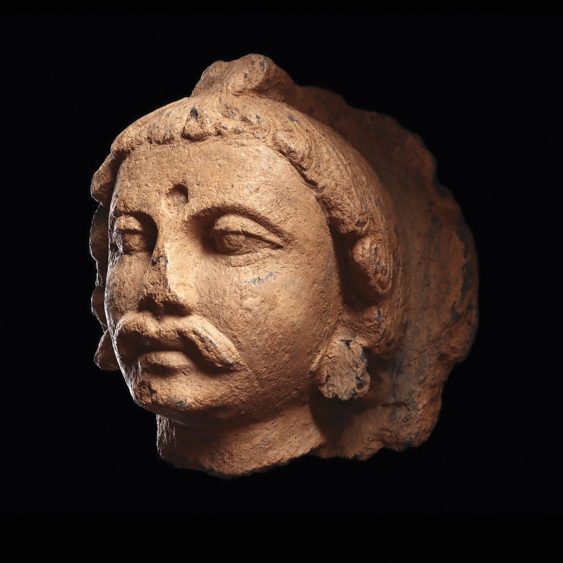 Gandharan Schist Head of a Bodhisattva with Urna and Mustache: Central Asia, Ancient Gandhara, present-day Pakistan or Afghanistan, ca. 100–400 CE. A large head of a bodhisattva carved in gray schist, broken from a once-standing or seated figure. The face i