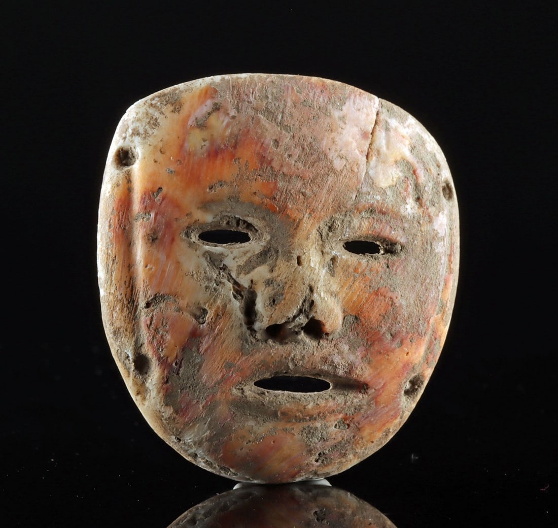 Fine Ancient Colima Spondylus Shell Mask Pendant: Ca. 300 BCE – 300 CE. Pre-Columbian, West Mexico, Colima culture, ca. 300 BCE to 300 CE. A carved spondylus shell (spiny oyster) panel formed as a miniature mask pendant, the rounded visage defi