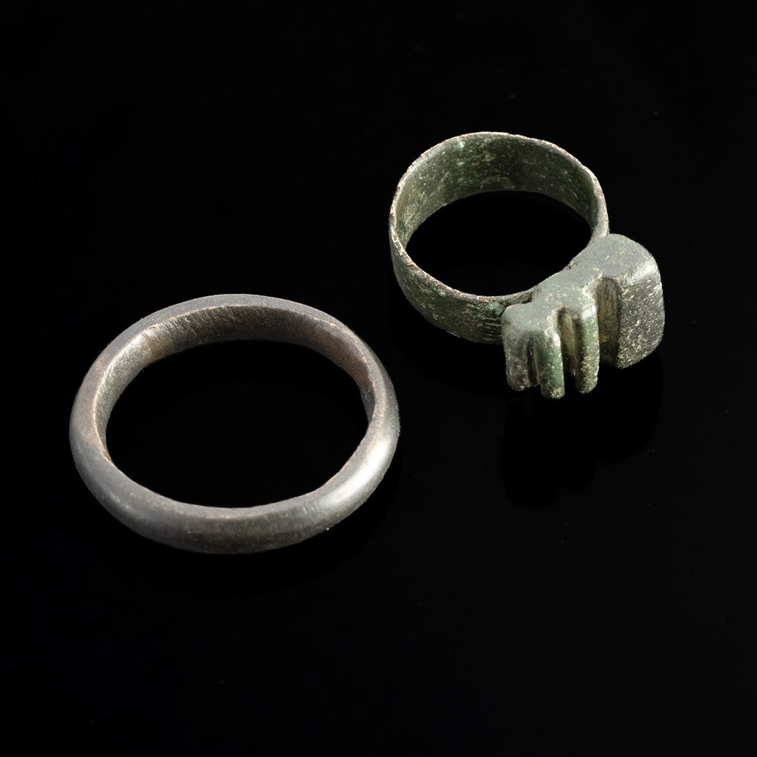 Roman Copper Key Ring & Leaded Bronze Ring: Roman, Imperial period, ca. 1–300 CE. A pair of ancient Roman finger rings preserving contrasting patinas, one deep green and earthen, the other a smooth gray-brown. The more petite example, cas