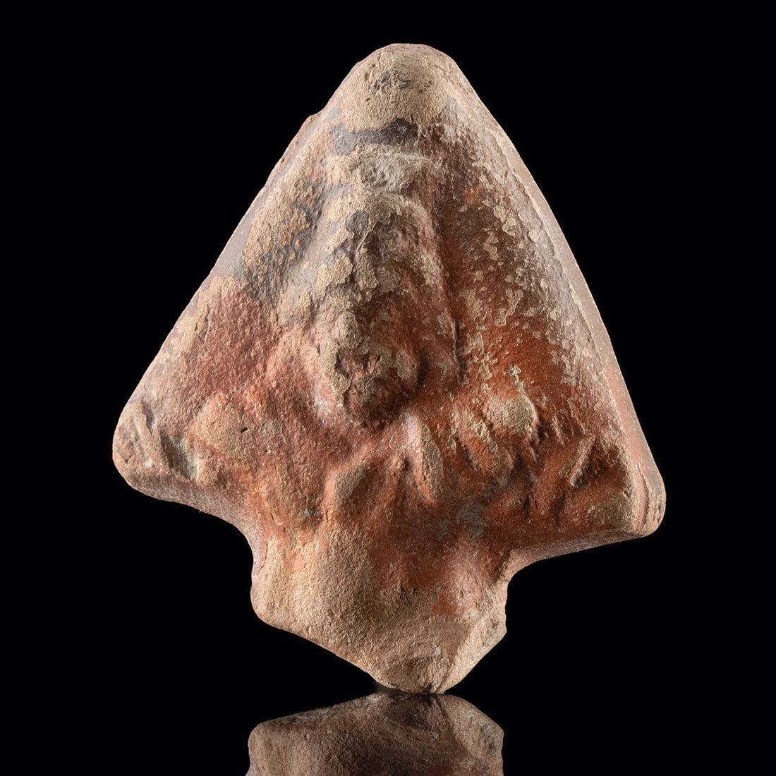 Egyptian Terracotta Lamp Finial - Zeus Serapis Bust: North Africa, Egypt, Greco-Roman period, ca. 100 BCE – 100 CE. A triangular terracotta finial broken from the shoulder of an oil lamp, its orange-buff fabric dressed in a red to brown slip that 