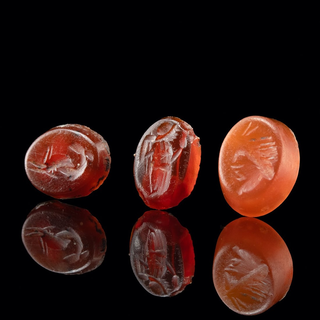 3 Roman Intaglios - Garnet Dolphin, Carnelian Pan & Glass Nike: Roman, Imperial period, ca. 50 BCE – 300 CE. A trio of miniature engraved gems, each cut in intaglio for setting into a finger ring and pressing into wax. The first, in red glass, carries a wing
