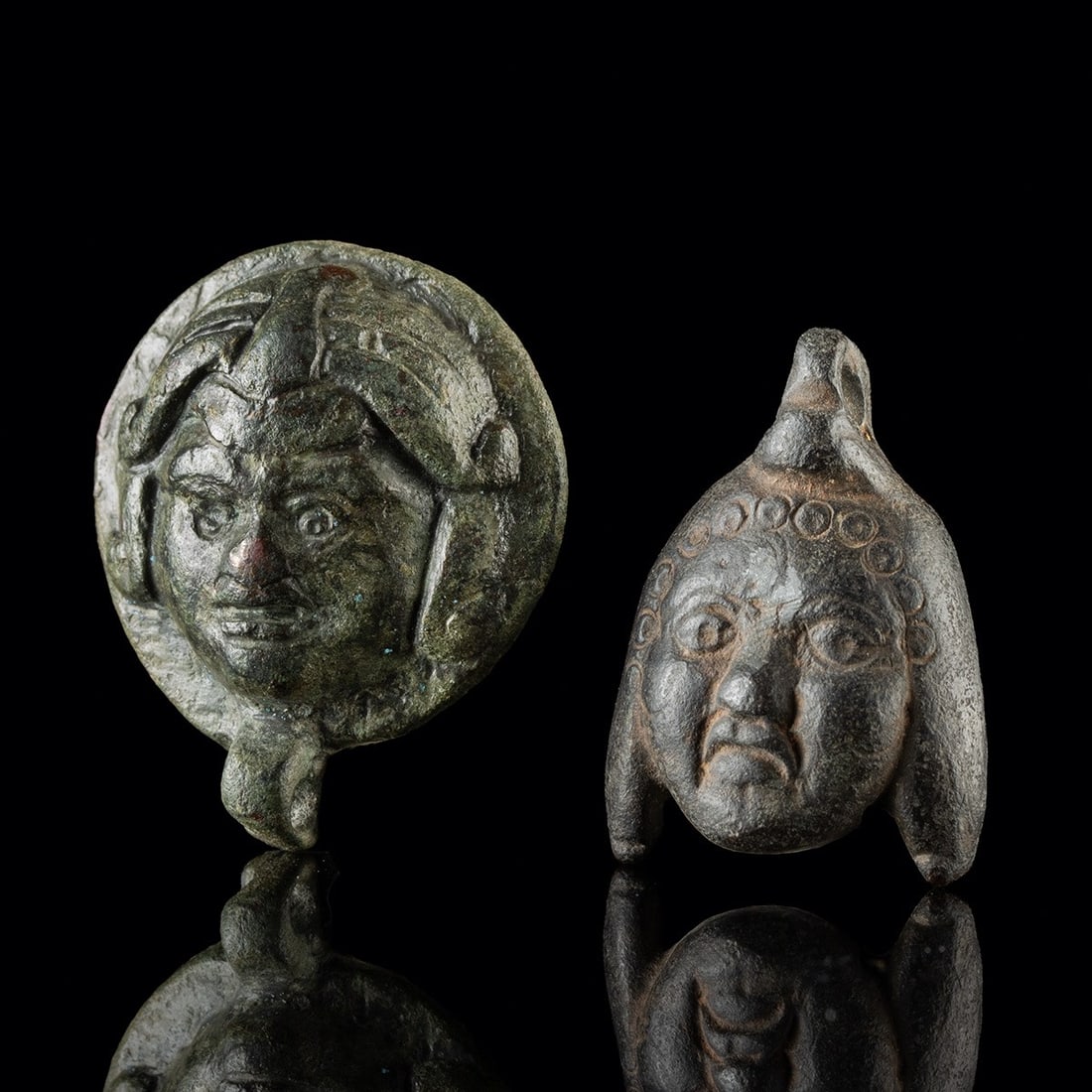 Two Roman Leaded Bronze Steelyard Weights - Medusa & Mithras: Roman, Imperial period, ca. 1–400 CE. A pair of small leaded bronze weights, each cast as a human face and fitted with an integral suspension loop for hanging from the arm of a steelyard balance