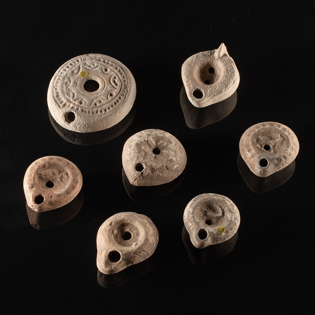 Seven Roman to Byzantine Holy Land Pottery Oil Lamps: Near East, Levant, Holy Land, Roman to Byzantine period, ca. 100–600 CE. A group of seven wheel-made and mold-made terracotta oil lamps in the closed Levantine tradition, each a squat, lenticula