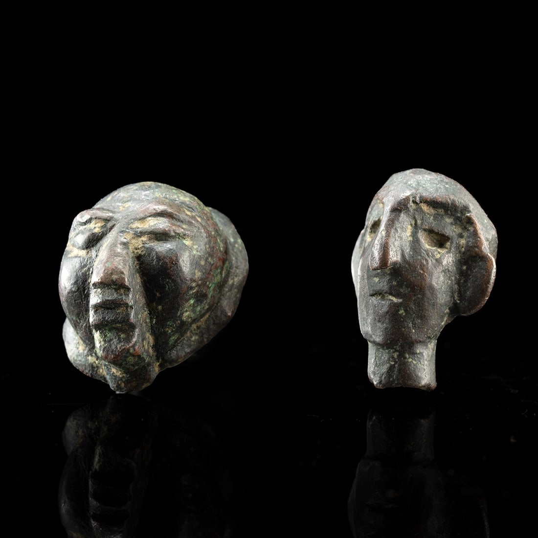 Near East Bronze Miniature Head and Maskette Pair, Ca. 1000 BCE - 300 CE: Eastern Mediterranean or Near East, ca. 1000 BCE – 300 CE. A pair of miniature cast heads, small enough to close a hand around, each reducing the human face to its essential geometry. The first,