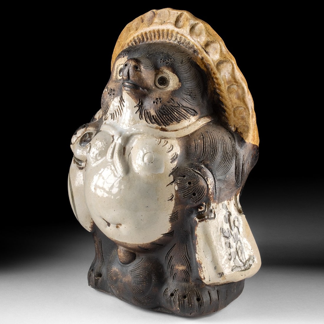 Mid-Century Japanese Shigaraki Pottery Tanuki Sculpture: Ca. 1934–1967 CE. East Asia, Japan, ca. mid 20th century CE. A stoneware tanuki figure in the classic Shigaraki tradition - wood-fired with natural ash glaze, flame markings, and coarse clay tex