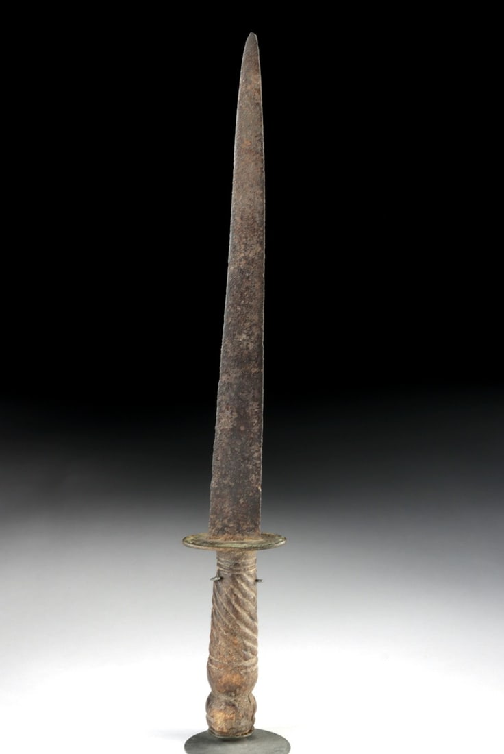 18th C. Iron Folk Dagger - Brass Guard, Wrapped Wood Grip: Europe or colonial Americas, ca. 1775–1875 CE. A slender hand-forged iron blade tapers to a needle point, its surface darkened by age and pitted with the granular patina of long-buried metal. A 