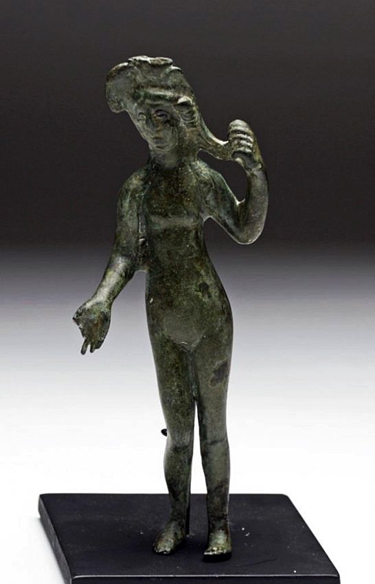 Roman Bronze Venus Figure: Rome, ca. 1st Century CE. A cast bronze statuette of the goddess Venus. Depicted naked with wind blown and long flowing hair. Standing in her classic pose, with left arm holding a braided strand of ha