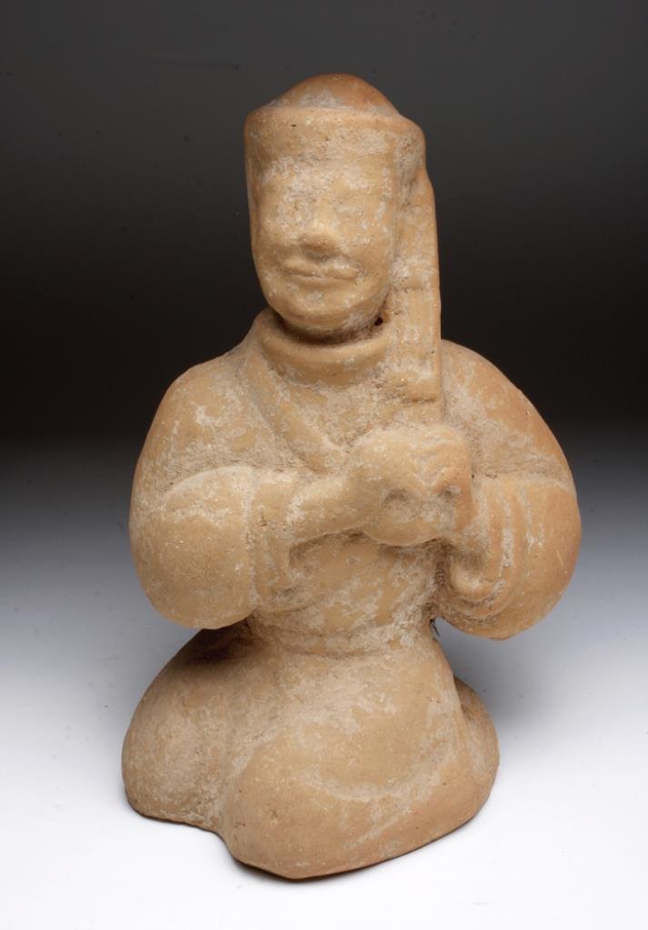 Chinese Han Dynasty Terracotta Seated Figure: China, Han Dynasty, Ca Ca. 206 BCE - 220 CE. Lovely and remarkably intact molded pottery seated male holding an object with both hands clutched to his chest. Wearing a draped garment and hat with a lo