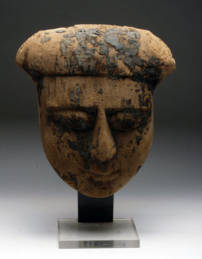 Egyptian Wood Mummy Mask - Saite Dynasty: Egypt, 26th Dynasty, Saite Dynasty, ca. 685 - 525 BCE. A carved wooden sarcophagus mask, with deep eyes, well formed nose, large cheeks, pursed lips, and headdress. Once painted, remnants of the black