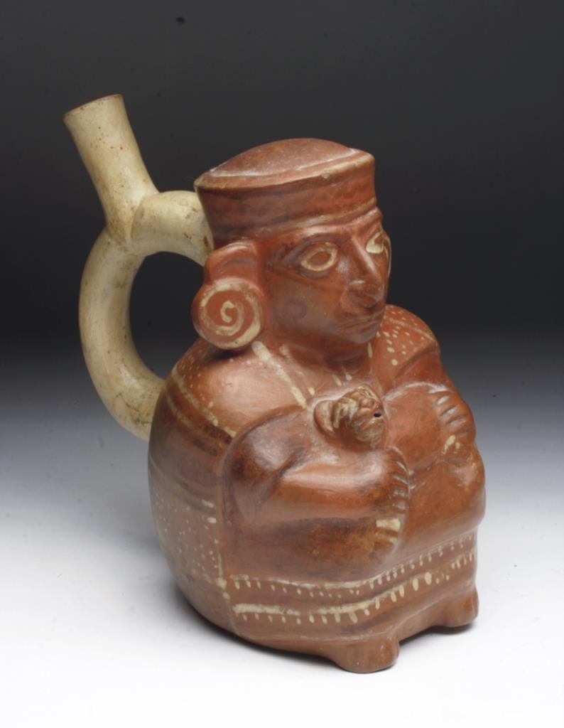 Adorable Moche Stirrup Vessel -Man and Cat: Northern Peru, ca. 400CE, Moche III, Pre-Columbian. This redware pottery vase is decorated in white over deep red slip and sports a lustrous, kaolin slipped stirrup spout. The vessel is in the form of
