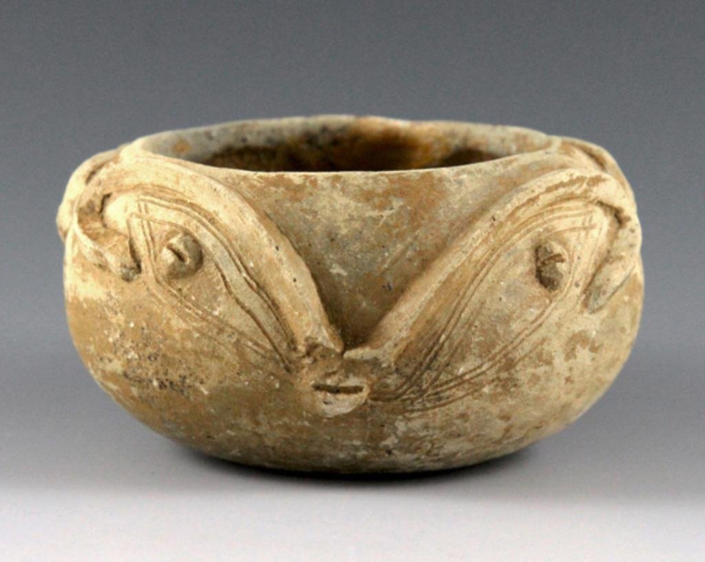 Pre-Columbian Tairona Face Vessel, Rare Type: From Colombia, ca. 1000 - 1550 CE. This squat terracotta bowl features applied decoration depicting faces on opposing sides, with dual-lined incised detailing. The buff color and designs on this vesse