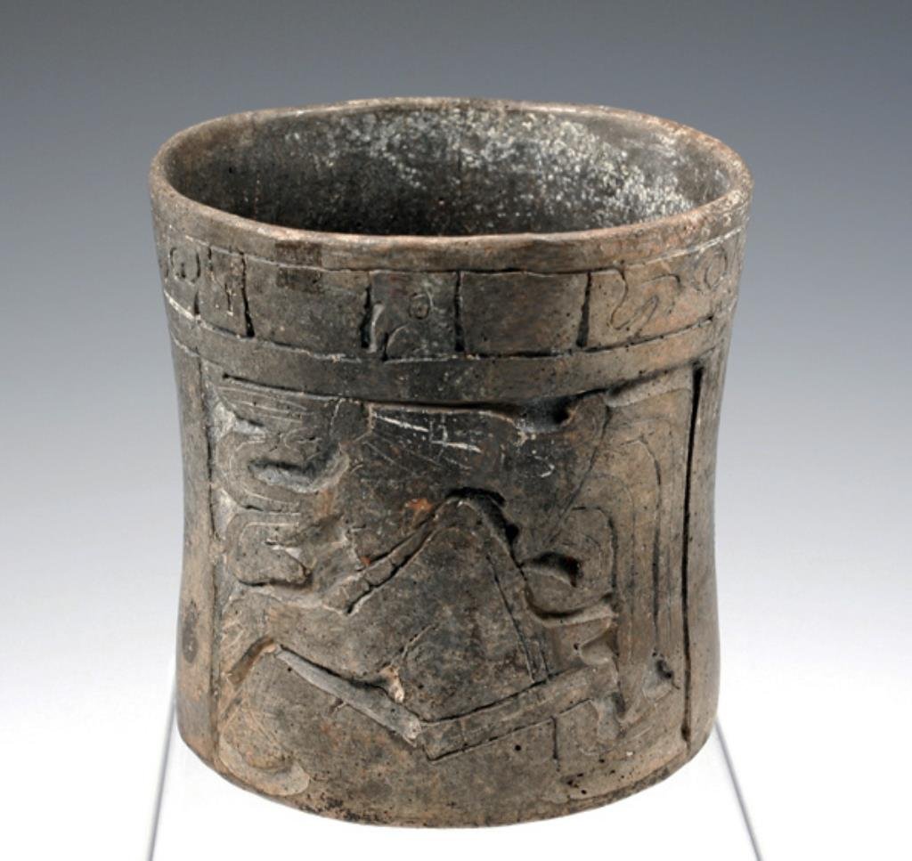 Pre-Columbian Mayan Carved Cylinder, ex-Peter Wray: A fine Pre-Columbian Maya carved vase, circa 600 - 900 CE. 5"H x ~5"W. This greyware cylinder exhibits a graceful form, with a gently corseted mid-section. Deeply carved panels on opposing sides conta