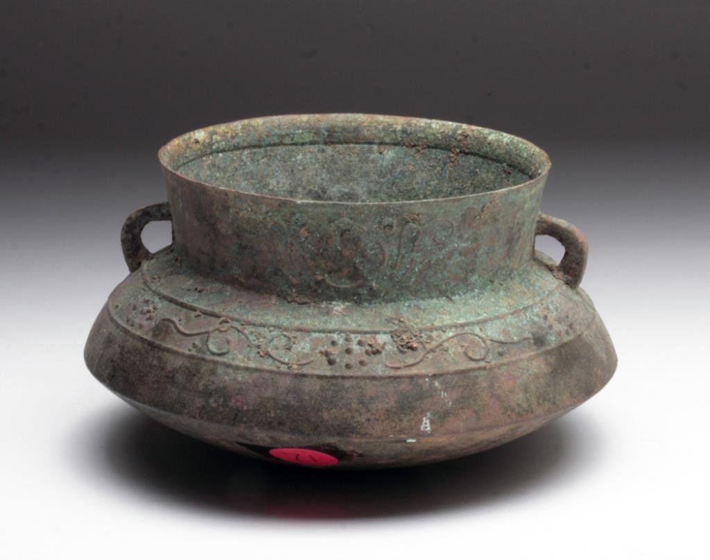 Dong Son Bronze Saucer Bowl: Cambodia, Dong Son culture ca. 500 BCE. Cast bronze bowl with saucer-like base and flared rim. Handles are connected to rim and shoulders of the vessel. Floral design around neck and shoulder. 6" diam
