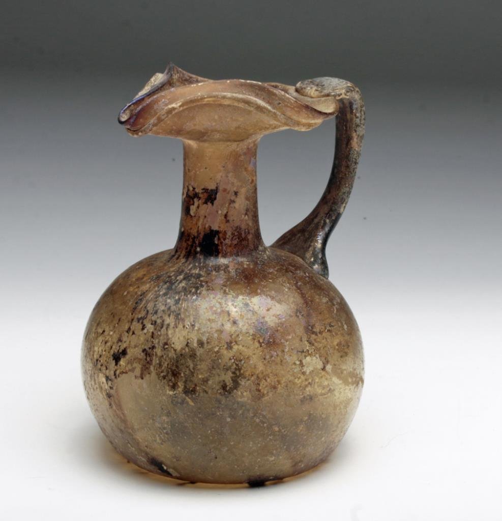 Beautiful Roman Glass Oinochoe: Rome, ca. 2nd - 3rd century CE. A very fine example of the glass take on the classic pottery form. Being composed of amber-colored glass, with large bulbous base, long thin neck, thin applied handle,