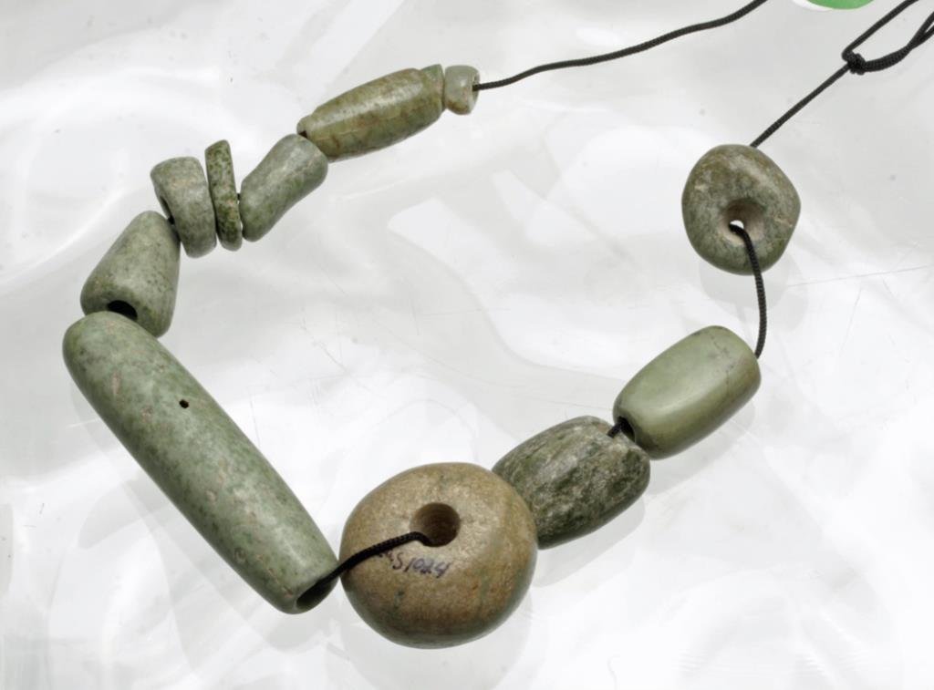Lot of 12 Ancient Mayan Jade Beads: Pre-Columbian, Mayan Territories, ca. 500-950 CE, Late Classic Period. This lot is composed of 12 jade beads including round, flat, and tubular-shaped forms. This example features a beautiful combinat