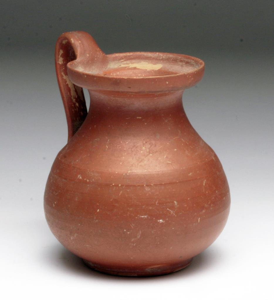 South Italic Messapian Redware Jar: Southern Italy, Daunian / Messapian Culture, ca. 5th - 4th century BCE. A finely crafted wheel made vessel with bulbous body, flared rim, and strap handle. Terracotta is slipped in a smooth red paint.