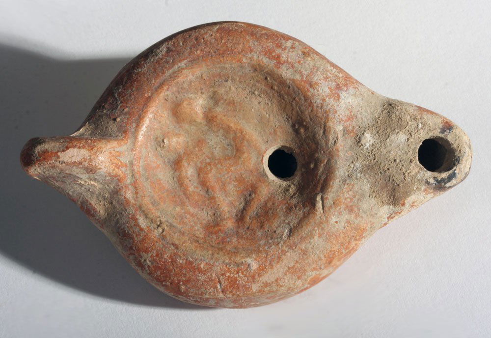 Roman Erotic Oil Lamp - Lover's Embrace: Rome, ca. 1st - 2nd century CE. Redware pottery lamp with center discus depicting two lovers embracing in intercourse in raised relief. Lamp and a central filling hole, spout with burn marks, and rais