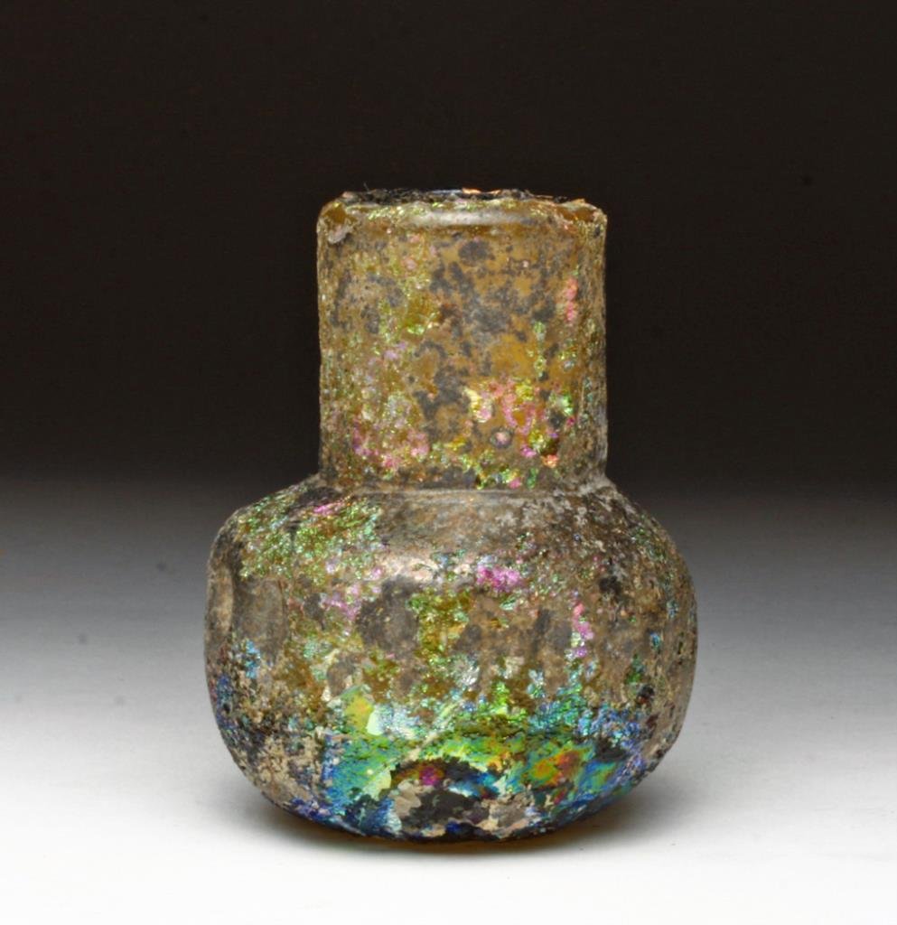 Beautifully Iridescent Roman Glass Unguent: Rome, ca. 1st - 2nd century CE. A small Roman glass vial with fascinating iridescence. This stout little bottle has vertically ribbed body and a cylinder neck. Green glass developed a wide range of ir