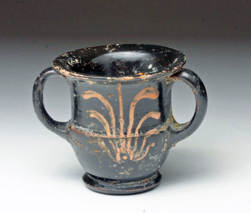 Greek Apulian Miniature Krater: Magna Graecia, Apulia, ca. 5th century BCE. A black-slipped miniature terracotta krater painted with red-figure palmettes on both sides. Low base, flared rim, and handles. Miniatures like this were no