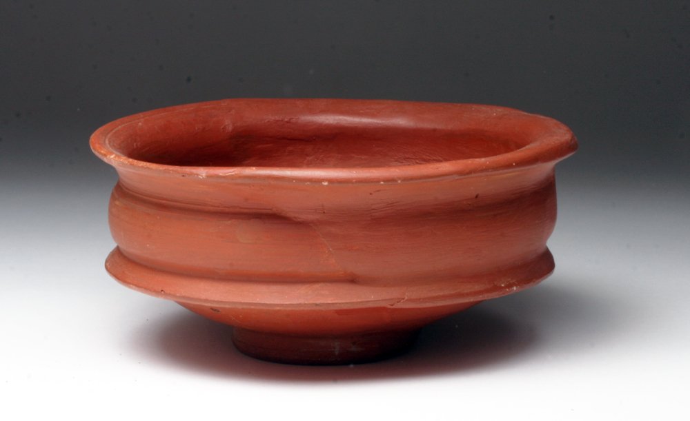 Roman Terra Sigillata Bowl: Rome, ca. 1st century CE. A beautiful redware bowl made in the terra sigillata technique. Bowl sits on low pedestal that gently tapers out to the body of the bowl, constructed with an upper and lower