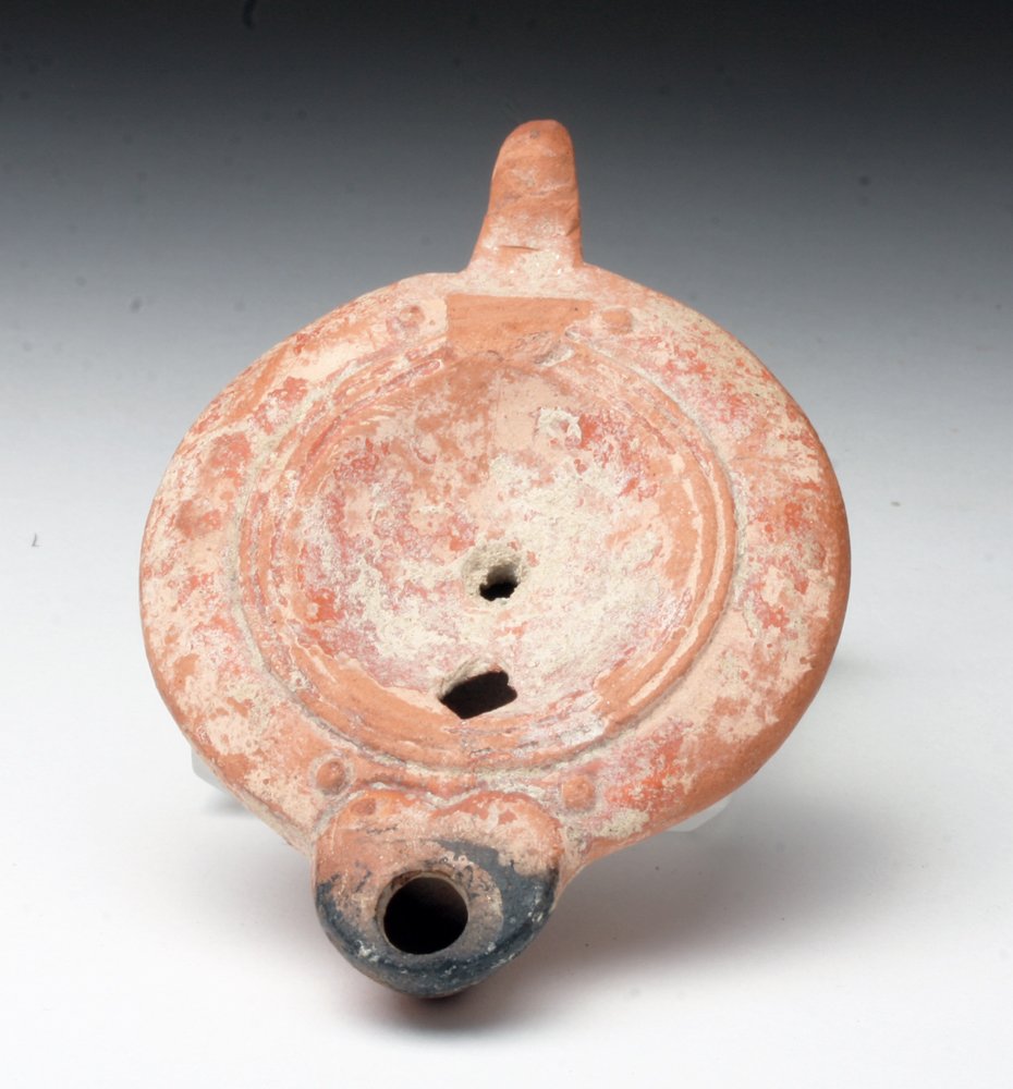 Ancient Roman Redware Lamp: Rome, ca. 1st century CE. Mold-made terracotta lamp in round form with small spout and handle. Two filling holes on face and one at spout. 3-1/4"L Provenance: Ex-Private Colorado Collection. All items