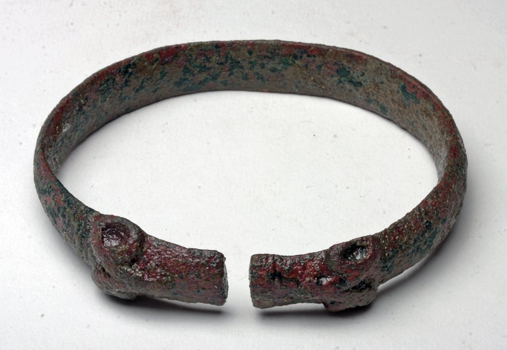 Large Bactran Bracelet -Ram Heads: Central Asia, ca. 1200 - 600 BCE. A large example of a cast bronze bracelet with dual ram heads at either side of opening. An interesting mixed patina of brown, red and green has developed on the piec