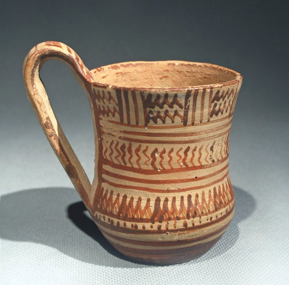 Late Geometric Greek Attic Single Handled Mug: Attic, Late Geometric II, late 8th cent. BCE. Mug on low foot with concave wall and high strap handle. Three friezes separated by bands. Metopes with zig-zags in the top frieze, sigmas in the central