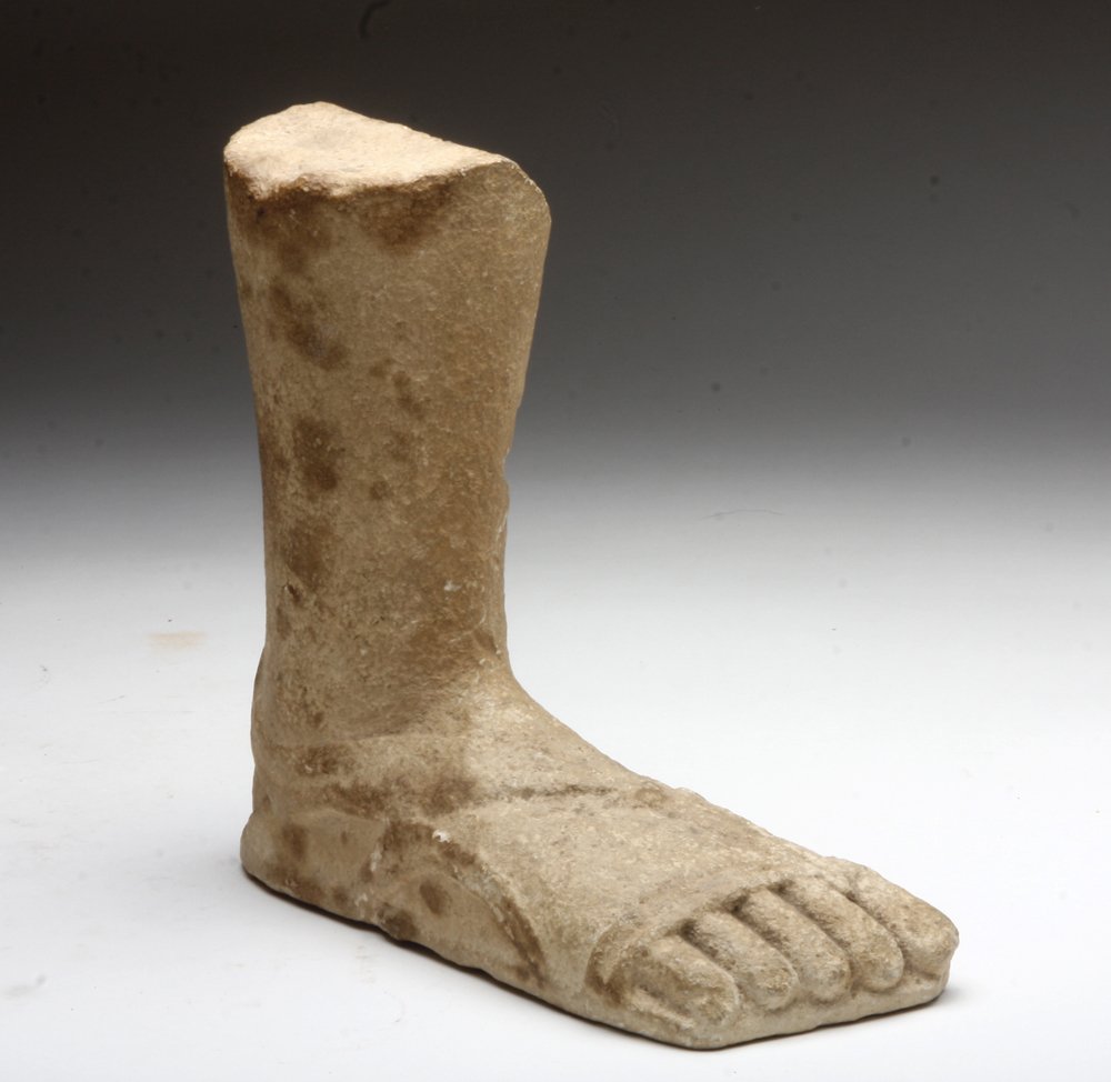 Hellenistic Greek Limestone Foot, ex-Sotheby's: Greece, Hellenistic Period, ca. 2nd century BCE, A carved limestone right foot and lower leg, likely from a larger seated statue. Depicted with carved sandal straps, long straight toes, ankle bones, a