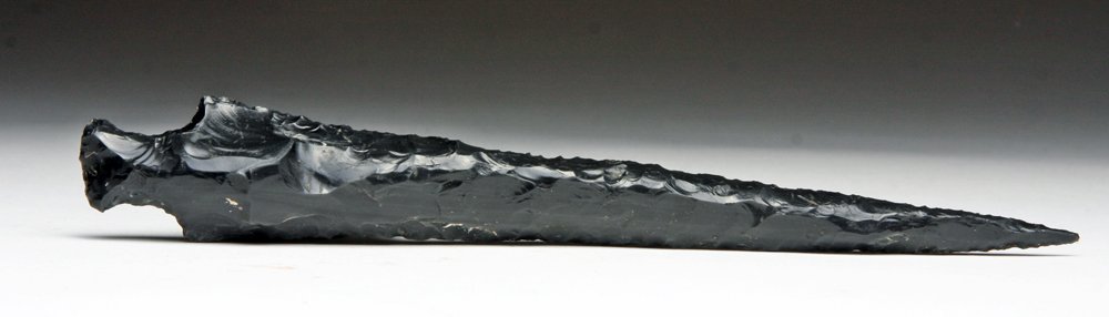 Another Colima Obsidian Stemmed Dagger: West Mexico, Ca 200 BCE to 200 CE. Another fine and quite lethal obsidian dagger made from volcanic glass. Deep black and with hundreds of knapped flakes removed to create this weapon. Twin nodes on e