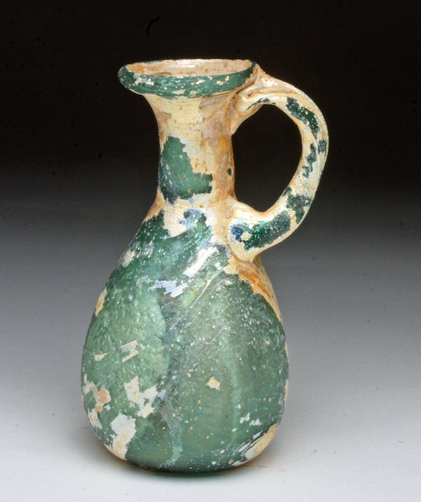 Roman Glass Flask, Twisted Handle: Rome, ca. 1st-2nd Century CE. A Roman blown aqua glass flask with twisted handle. The wide body tapers into a cylindrical neck with funnel spout. A twisted glass strap handle is attached from base of 