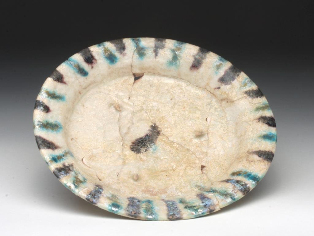 Beautiful Islamic Kashan Pottery Plate: Iran, 13th to 14th century. Gorgeous pottery plate on short foot, covered with white glaze and highlighted with added blue and brown pigment impressed design in center. 6-1/8" D. Provenance: Ex-Smith 