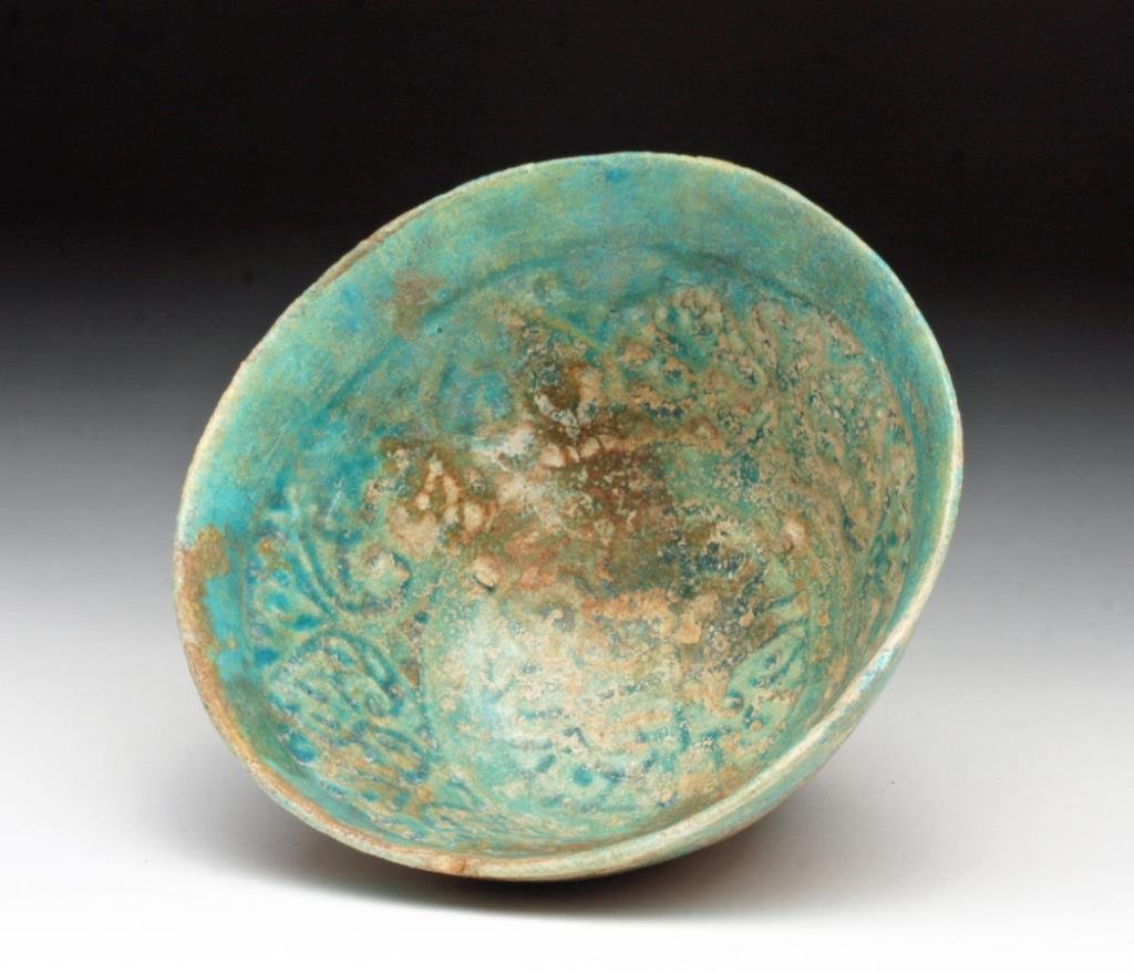 Islamic Blue Glazed Bowl, possibly Kashan: Iran, Ca 12th to 14th century, possibly Kashan region. Beautiful blue-green ceramic bowl on short foot, impressed in the center with floral patterns. Areas of silvery iridescence! 4-7/8" D. Provenance